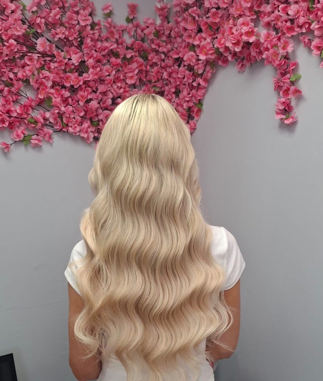 Platinum blonde Hollywood-wave hair extensions in front of the pink blossom wall at Luxe Hair Midleton